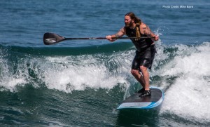 Male Stand-up Paddle (SUP) surfer with tattoos, long hair, and b